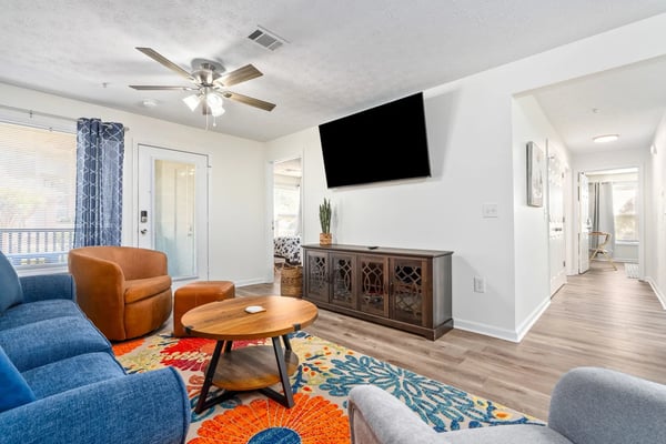Bright living room with blue and orange upholstered seating, wooden coffee table, wall-mounted TV, and dark wood media console